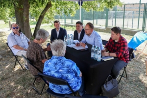 na zdjęciu osoby siedzące przy stole, na świeżym powietrzu, rozmawiające