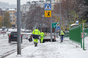 Na zdjęciu zaśnieżony chodnik oraz pracownicy MPGK posypujący go solą
