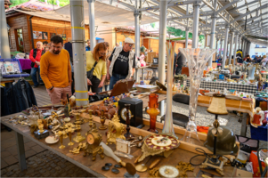 Na zdjęciu stoły z bibelotami do sprzedaży, obok przyglądający się im kupujący