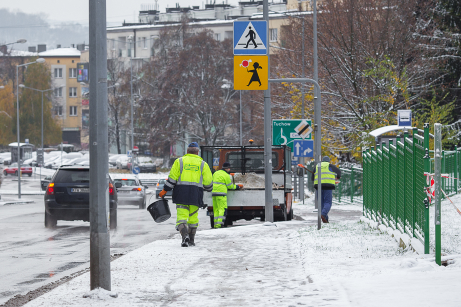 Na zdjęciu zaśnieżony chodnik oraz pracownicy MPGK posypujący go solą